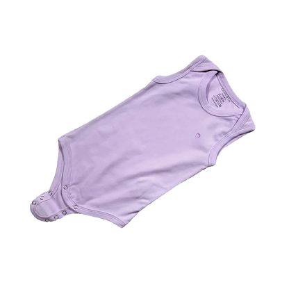 Purple baby onesie on a gray surface with baby-themed toys and 'Ghaida & Co' branding.
